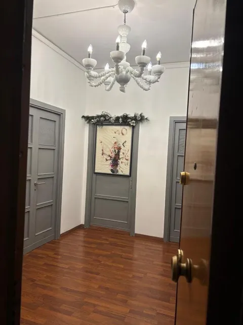 Il corridoio con il lampadario bianco, le porte grigie delle camere e un quadro