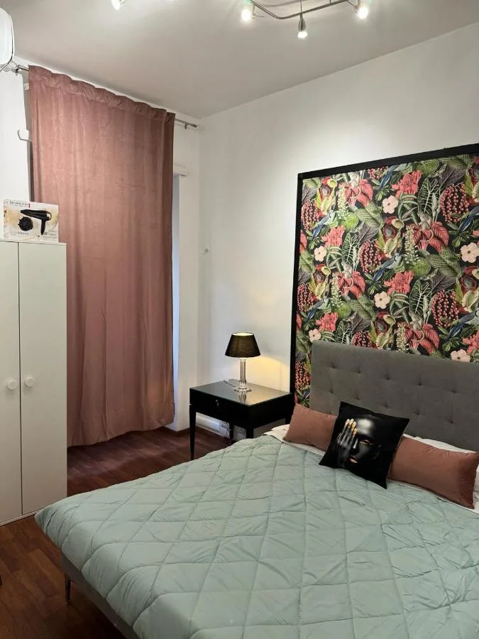La camera matrimoniale: il letto con il copriletto verde acqua, la parete con i fiori e le tende rosa